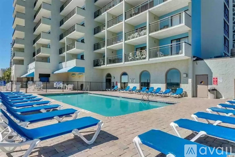A pool area with sun loungers in front of a white building.