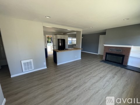 A living room with a fireplace and a kitchen in the background.