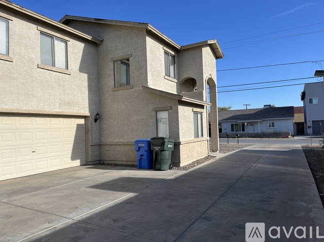 A beige house with a blue and green trash bin in front.