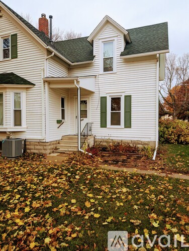 A white house with green shutters and a grey roof.