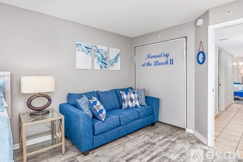 A living room with a blue couch and a painting of a beach scene.