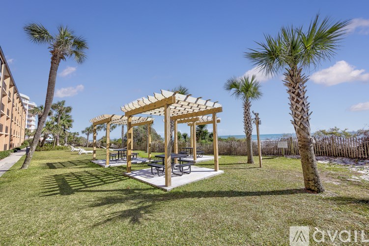 A wooden pavilion is surrounded by palm trees in a grassy area.