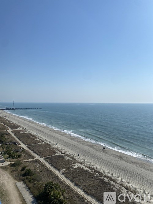 A beach with a pier in the distance under a clear blue sky.