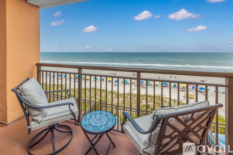 A balcony with two chairs and a table overlooking a beach.