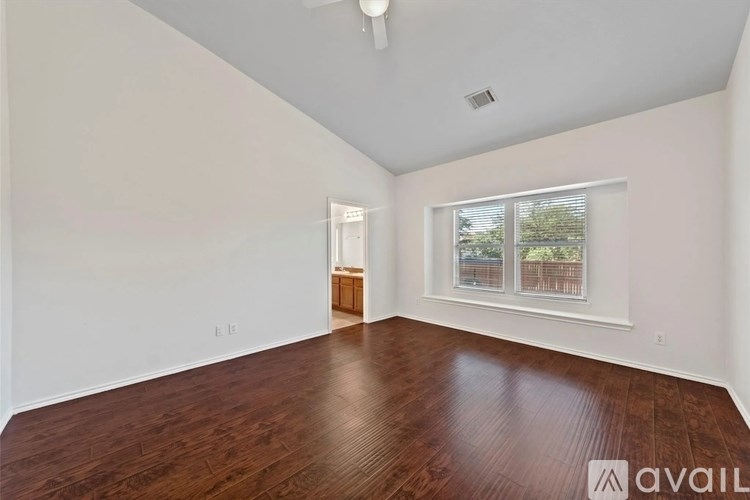 A spacious room with wooden flooring and a window with a view of trees.