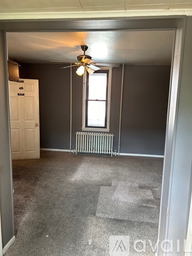 A room with a ceiling fan and a window with a radiator beneath it.