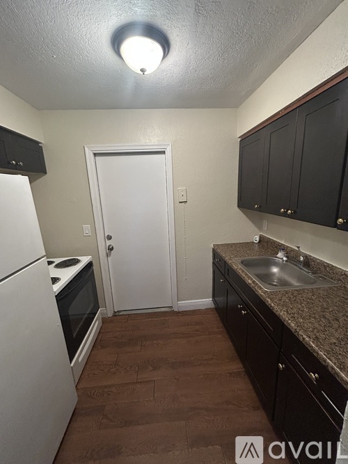 A kitchen with brown flooring, white appliances, and black cabinets.