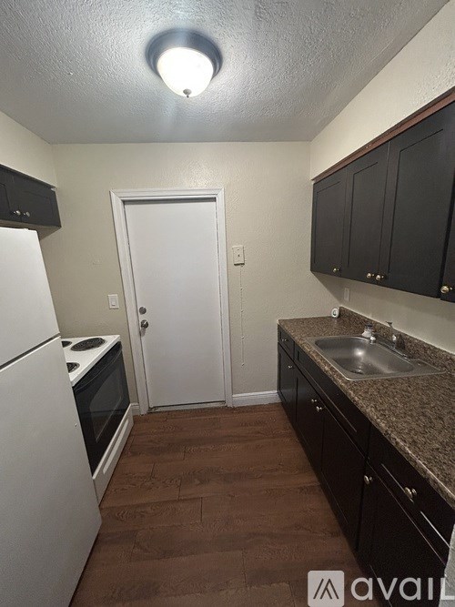A kitchen with brown flooring, white appliances, and black cabinets.