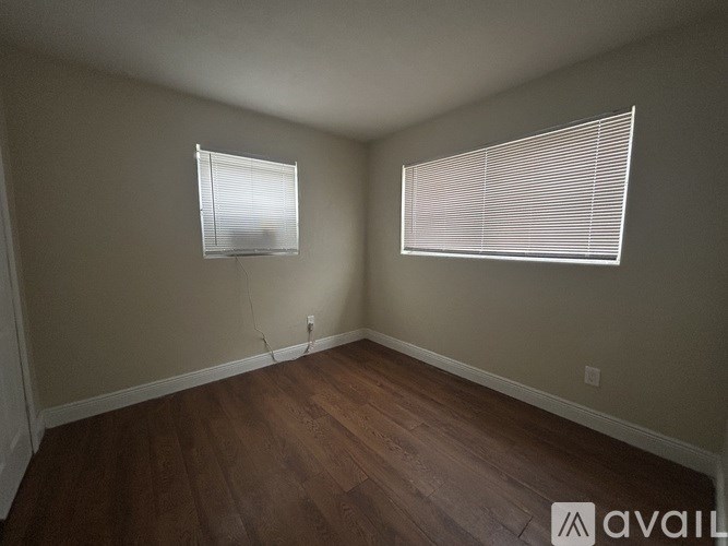 A room with wooden floors and two windows with blinds.