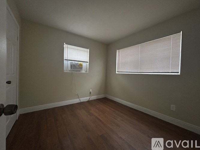 A room with wooden floors and two windows with blinds.