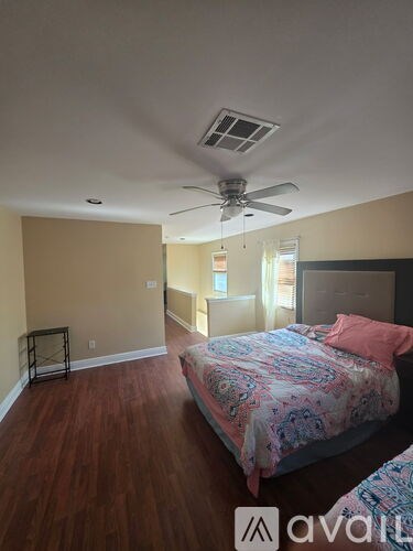 A bedroom with a bed, a ceiling fan, and a wooden floor.