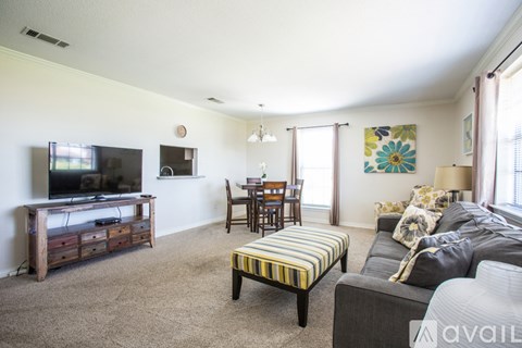 A living room with a grey couch, a striped ottoman, a wooden entertainment center, and a dining table with chairs.