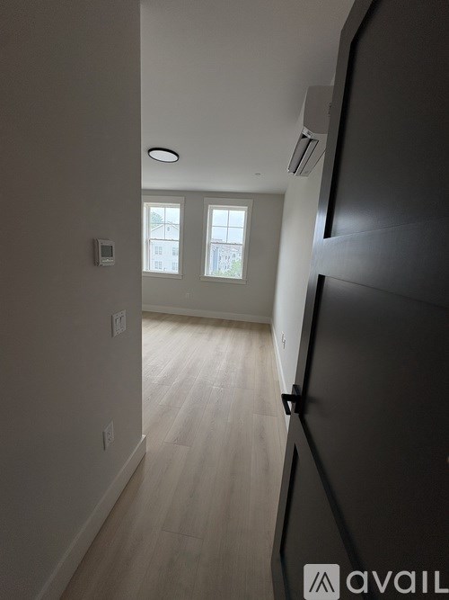 A hallway with a black door on the right and a window with a view of a building in the distance.