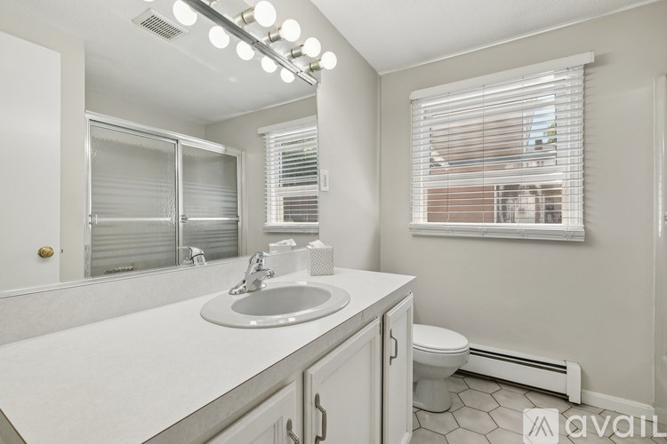 A bathroom with a sink, mirror, toilet, and window.
