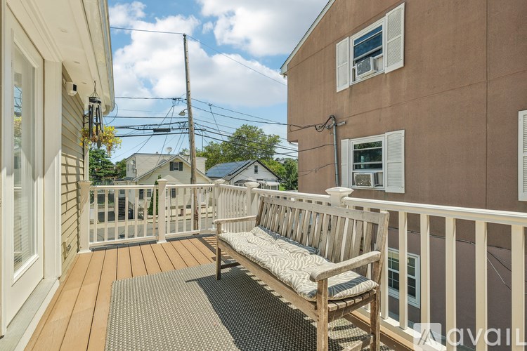A wooden bench sits on a deck with a view of a house and trees.