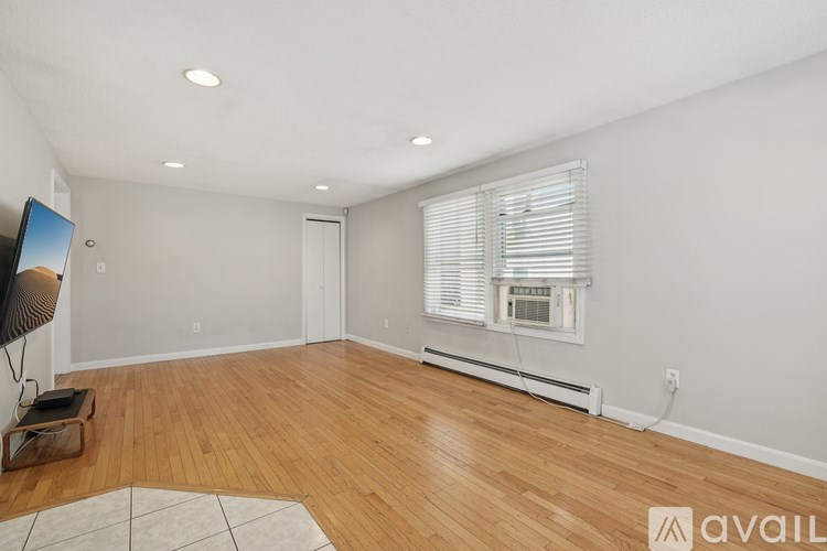 A spacious room with wooden flooring and a window with blinds.