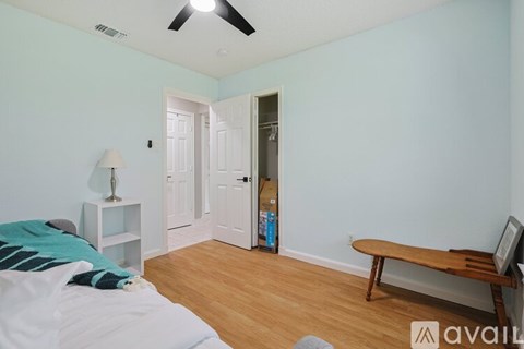 A bedroom with a bed, a nightstand with a lamp, a bench, and a door leading to another room.