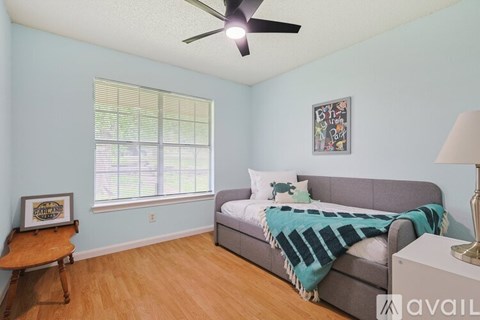 A bedroom with a bed, a couch, a ceiling fan, and a window with blinds.