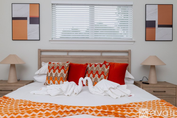 A bedroom with a white bed and orange and white pillows.
