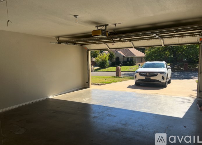A car is parked in a garage with a view of a house and trees outside.