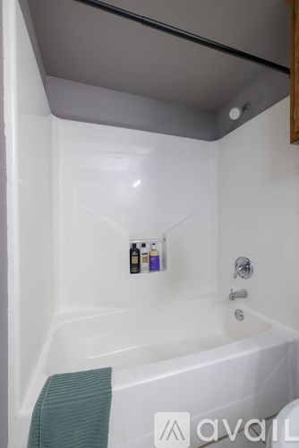 A white bathtub with a green towel and two bottles of shampoo and conditioner on the side.