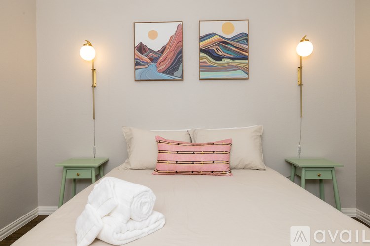 A bedroom with a bed, two lamps, and two paintings on the wall.