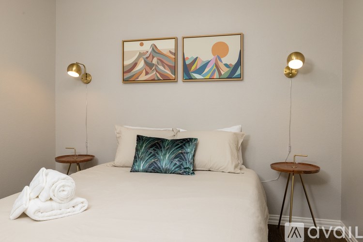 A bedroom with a bed, two lamps, and two paintings on the wall.