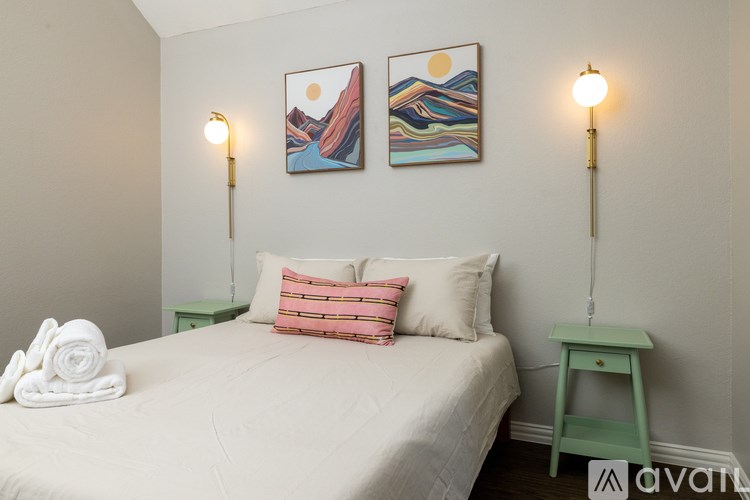 A bedroom with a bed, two lamps, and two paintings on the wall.