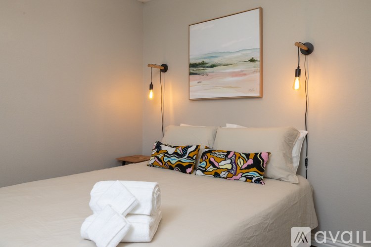 A bedroom with a bed, two lamps, and a painting on the wall.