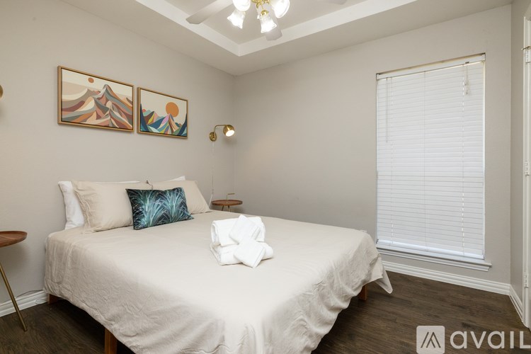 A bedroom with a bed, two pillows, a blanket, a window with blinds, a ceiling light, and two wall art pieces.
