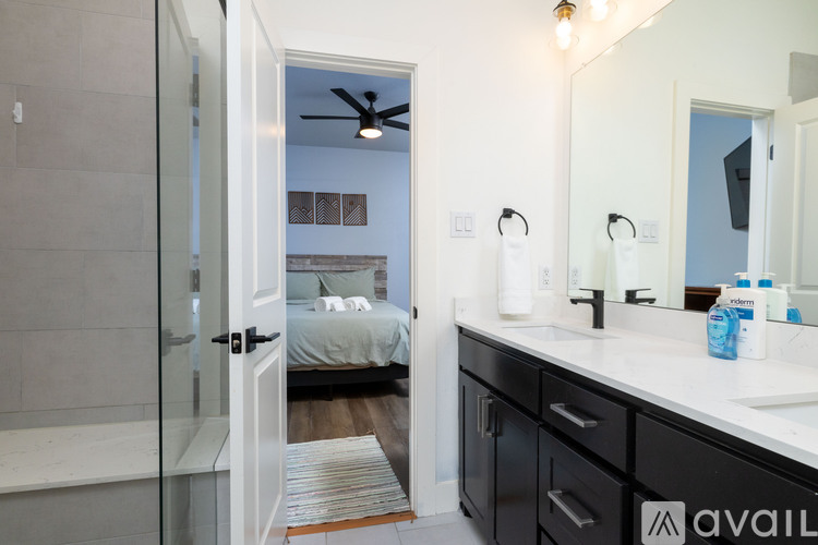 A bathroom with a mirror, sink, and a bedroom with a bed and a ceiling fan.