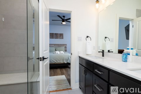 A bathroom with a mirror, sink, and a bedroom with a bed and a ceiling fan.