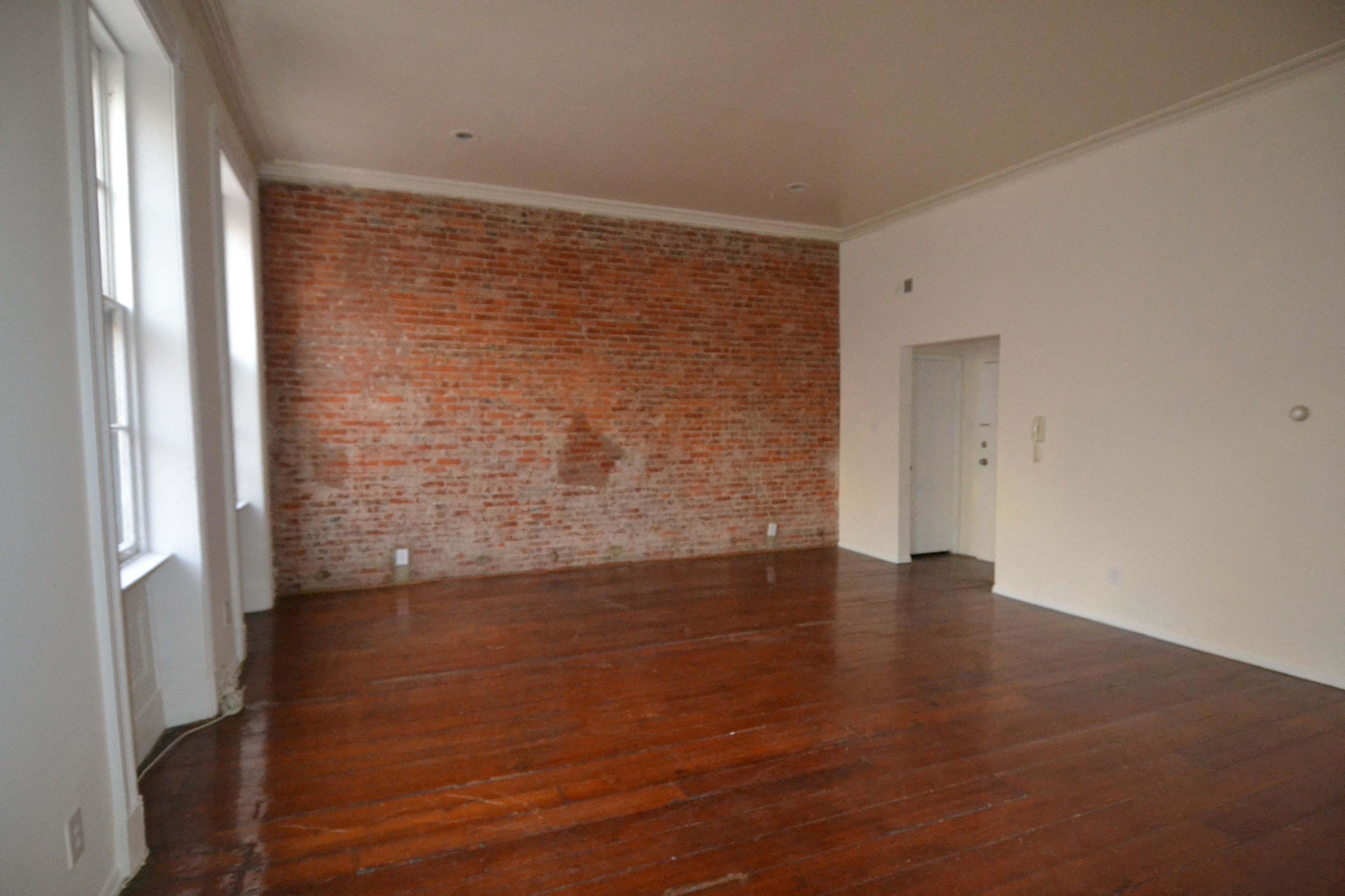an empty living room with wooden floors and a brick wall