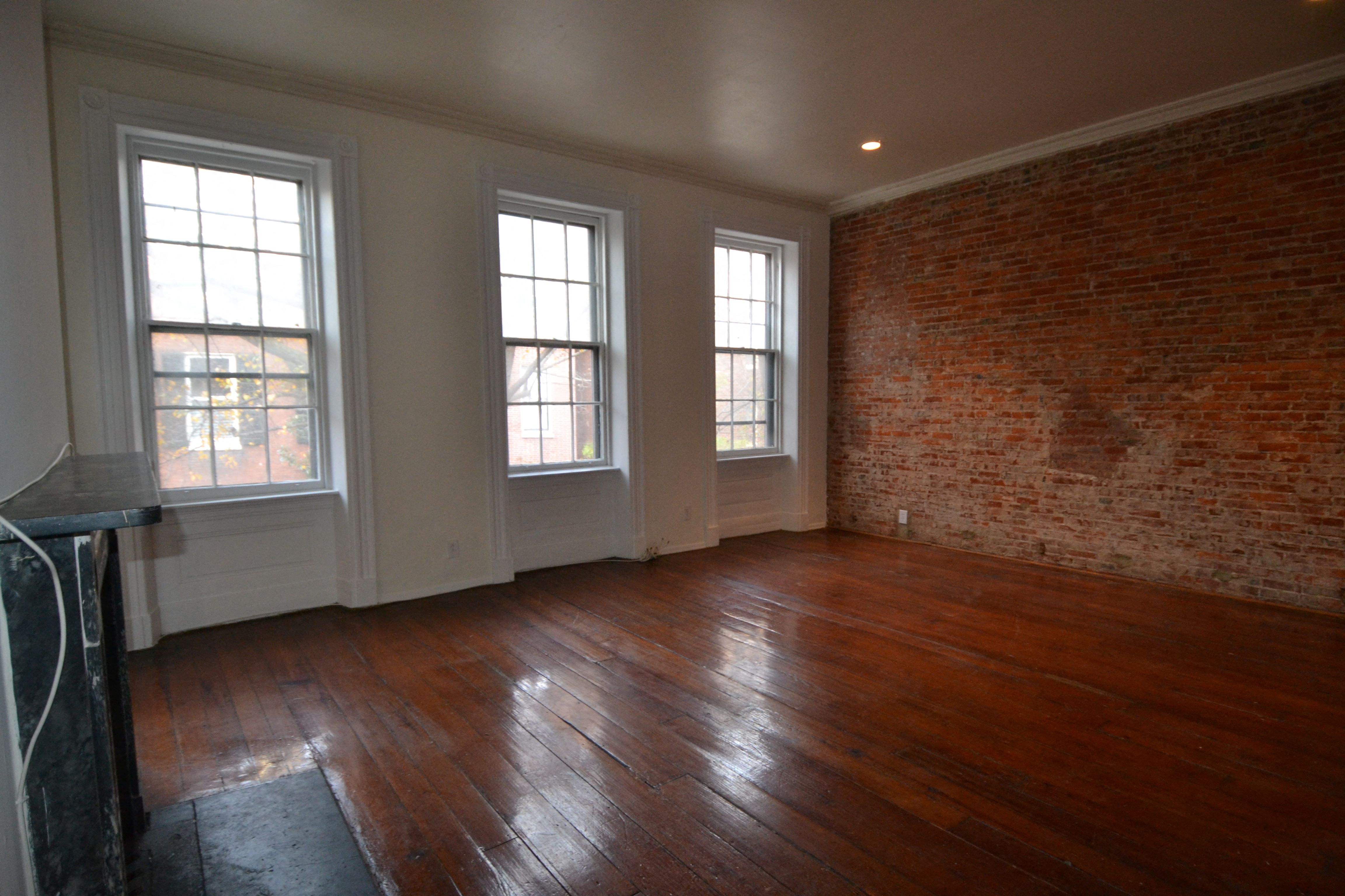 an empty living room with a brick wall and wooden floors