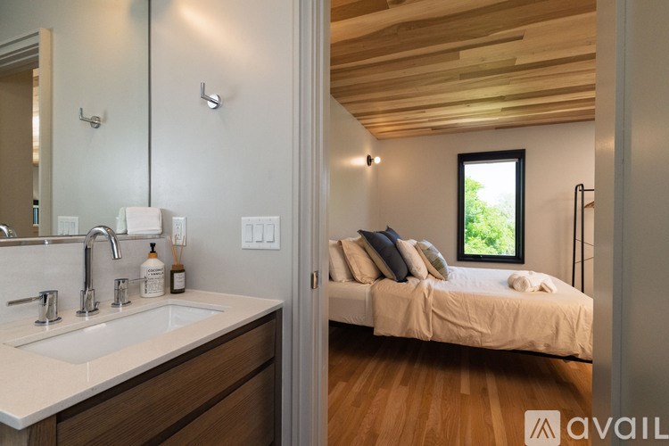 A bathroom with a double sink vanity and a bedroom with a bed and a window.