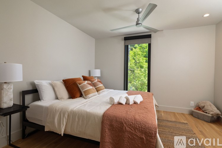 A bedroom with a bed, pillows, a blanket, a ceiling fan, and a window with a view of trees outside.