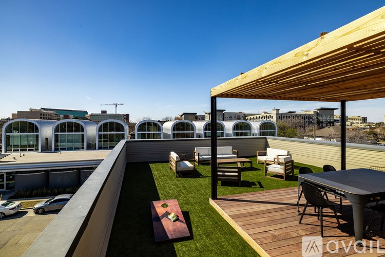 A wooden deck with a table and chairs overlooks a grassy area and a parking lot.