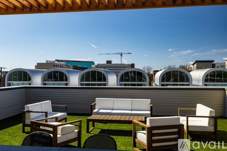 A patio with white chairs and a wooden table is set up on a rooftop.