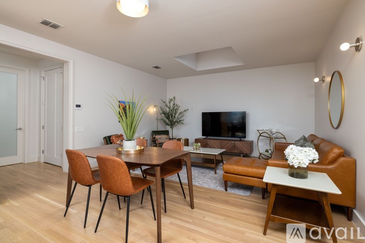 A living room with a brown leather couch, a wooden dining table with chairs, and a television.