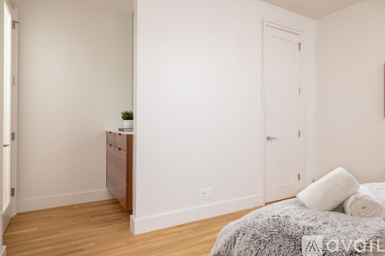 A small bedroom with a bed, nightstand, and a plant.