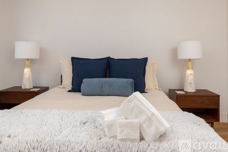 A bed with white and blue bedding and two white lamps on either side.