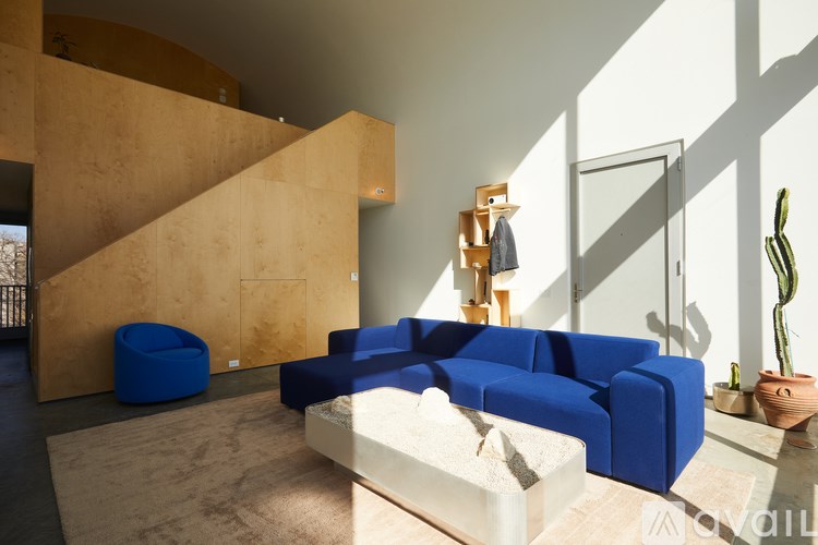 A blue sofa sits in a room with a tan wall and a wooden staircase.
