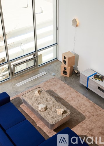 A room with a blue couch, a table with a glass container and a blue container with a white logo on it.
