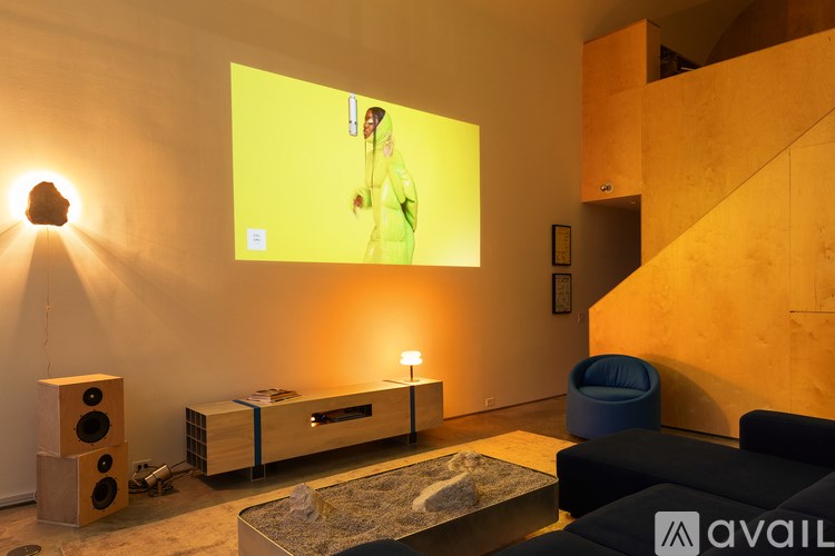 A woman in a green dress is on a yellow screen in a room with a speaker and a blue chair.