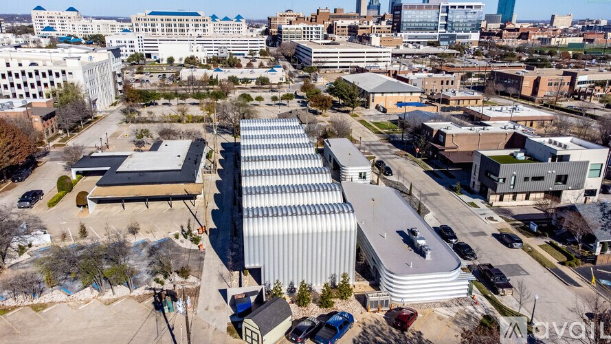 A large industrial building with a curved roof is surrounded by other buildings and vehicles.
