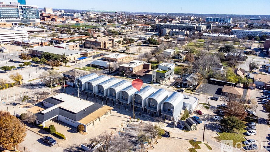 A large building with a red roof is surrounded by other buildings and trees.