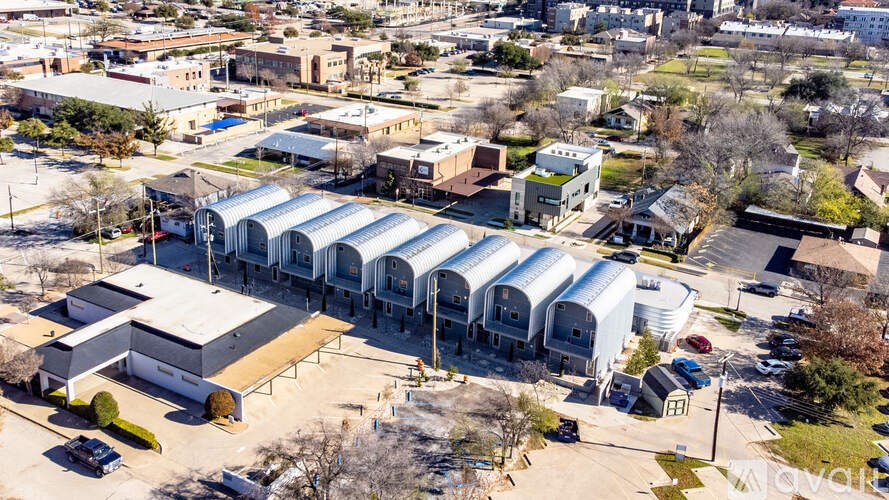 A large industrial building with a long white roof is surrounded by smaller buildings and cars.