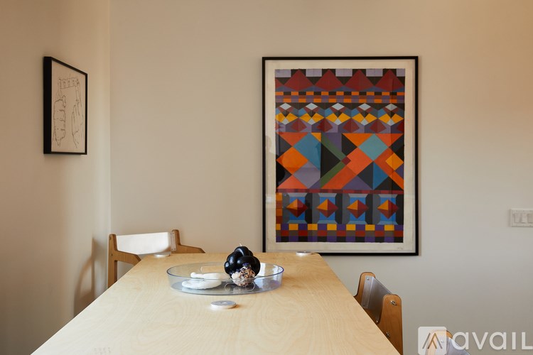 A table with a bowl and a vase on it with a picture in the background.