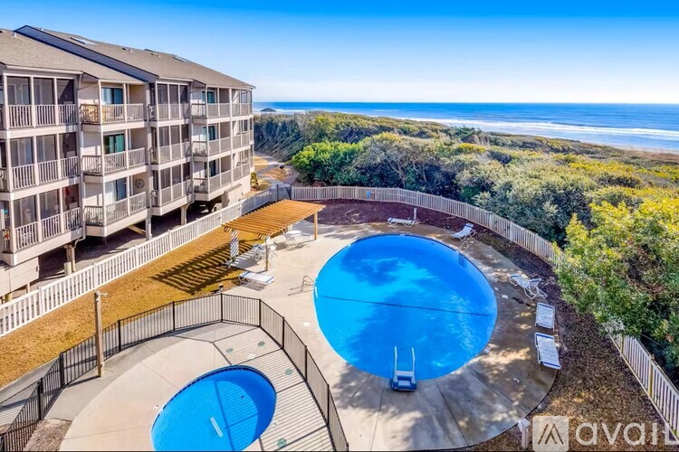 A large swimming pool with a hot tub is surrounded by a fence and a building with balconies.