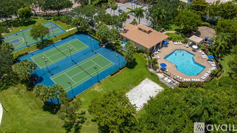 An aerial view of a tennis court surrounded by trees and a pool.
